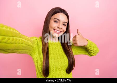 Foto ritratto di ragazza cute giovane fare selfie streaming pollice su spazio vuoto indossare trendy vestito verde isolato su sfondo di colore rosa Foto Stock