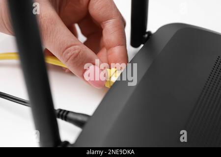 Donna che collega il cavo al router al tavolo bianco, primo piano. Comunicazione Internet wireless Foto Stock