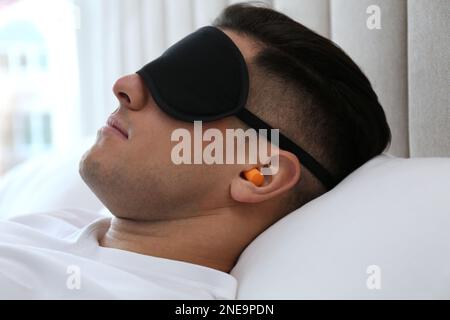 Uomo con tappi auricolari in schiuma e maschera che dorme a letto, primo piano Foto Stock
