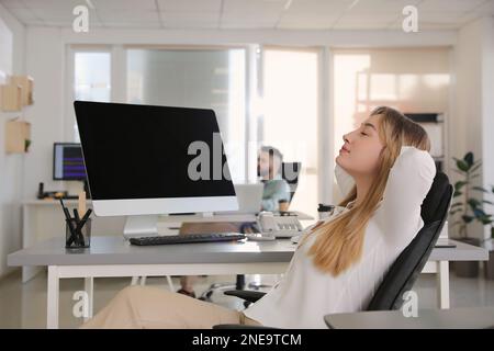Giovane donna d'affari che si rilassa in sedia da ufficio sul posto di lavoro Foto Stock