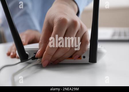 Donna che collega il cavo al router al tavolo bianco, primo piano. Comunicazione Internet wireless Foto Stock