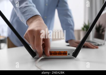 Donna che collega il cavo al router al tavolo bianco in interni, primo piano. Comunicazione Internet wireless Foto Stock