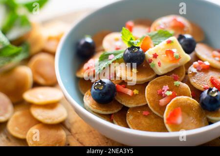 Mini frittelle di cereali con burro e frutta rossa in un recipiente. Foto Stock