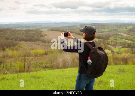 Il modello femminile di mezza età fa foto di montagne sullo smartphone Foto Stock