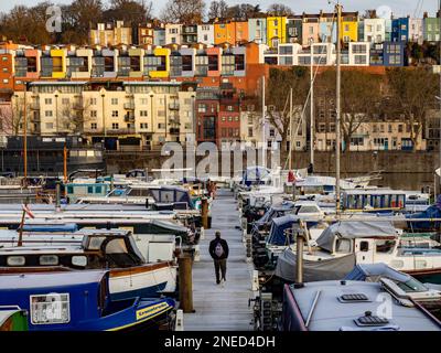Vista posteriore dell'uomo che cammina lungo il molo di legno coperto di ghiaccio di Bristol Marina. Con case a schiera colorate in lontananza. Foto Stock