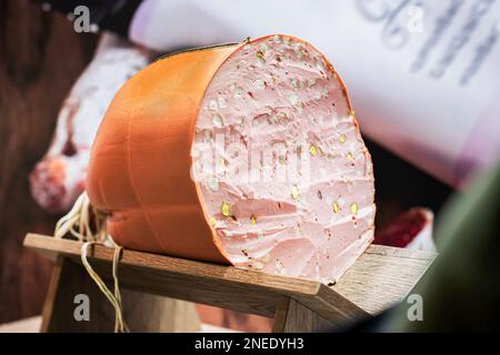 Salsiccia di Mortadella appetitosa biologica con olive in legno primo piano, vera scena nel mercato alimentare, focalizzazione selettiva Foto Stock