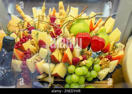 Composizione della drogheria in una vetrina da un assortimento di formaggi a fette, uva e altri frutti, noci. Un regalo delizioso per i tuoi cari. Sof selettivo Foto Stock