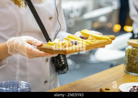 Tavola di legno con formaggi assortiti nelle mani della ragazza promotore, scena reale nel negozio di alimentari, fuoco selettivo Foto Stock