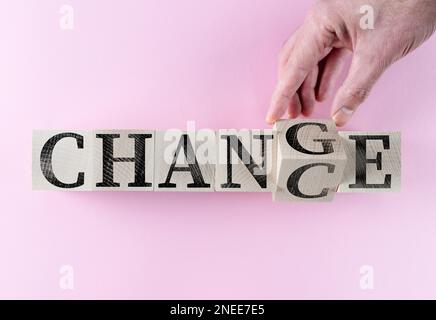 Mano che trasforma il cambiamento di parola IN OCCASIONE su blocchi di legno contro sfondo rosa Foto Stock