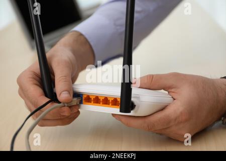 Uomo che collega il cavo al router al tavolo di legno, closeup. Comunicazione Internet wireless Foto Stock