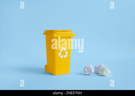 Contenitore giallo per raccolta rifiuti carta e carta stropicciata, isolato su sfondo blu con spazio copia, concetto di riciclaggio dei rifiuti Foto Stock