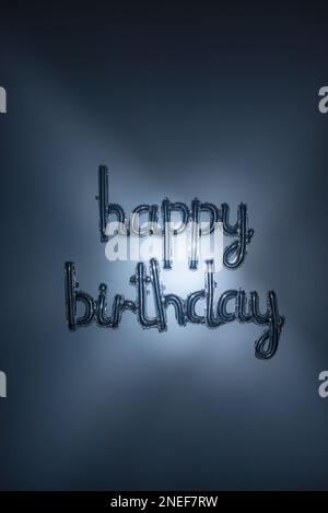 Scritta in argento con palloncino da compleanno e luce blu da sogno. Lettere in foglio su sfondo verticale. Saluto metallico, decorazione per feste, invito all'evento Foto Stock