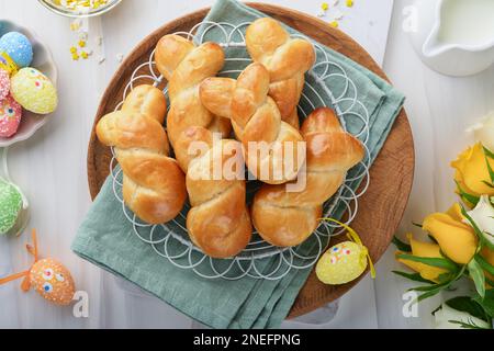 Colazione di Pasqua, concetto di Holliday. Panini di coniglietto pasquale con cannella a base di pasta di lievito con smalto arancione, decorazioni pasquali, uova colorate Foto Stock