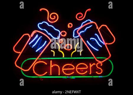 Luce al neon modellata nella parola “Cheers” con due pinte di birra sopra di essa. Foto Stock