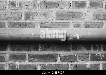 Tipici tubi metallici comuni che corrono lungo una parete di mattoni in bianco e nero. Foto Stock