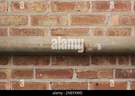 Tipici tubi metallici comuni che corrono lungo una parete di mattoni. Foto Stock