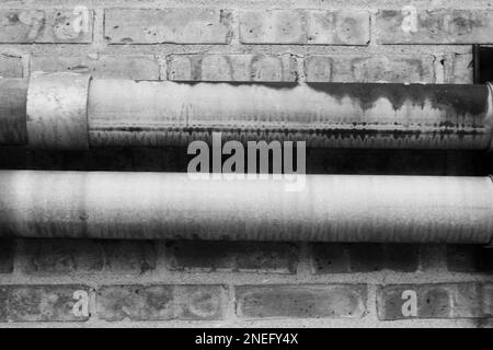 Tipici tubi metallici comuni che corrono lungo una parete di mattoni in bianco e nero. Foto Stock