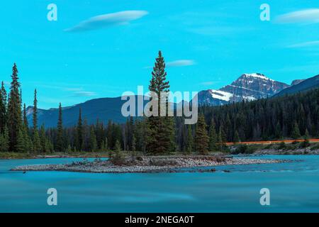 Il fiume Athabasca di notte con sentieri stellari e luci rosse lungo l'autostrada con il Monte Edith Cavell sullo sfondo, il parco nazionale Jasper, Canada. Foto Stock