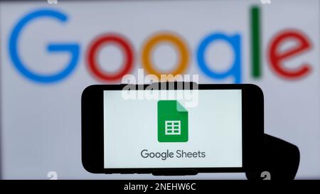 In questa immagine, il logo di Google Sheets viene visualizzato sullo schermo di un telefono cellulare con un logo Google sullo sfondo. Foto Stock