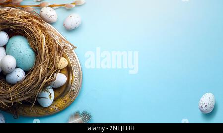 Biglietto di auguri di Pasqua o sfondo banner con uova di Pasqua e fiori primaverili su tavolo blu Foto Stock