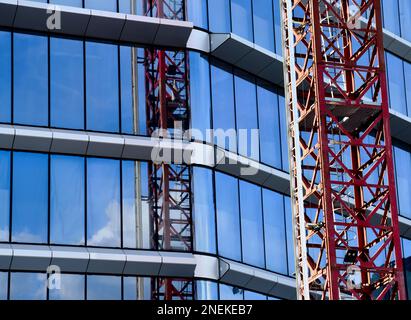 edificio in vetro con vista dall'alto con cielo blu e gru a torre in acciaio rosso che si riflettono nelle finestre. architettura moderna. vista astratta. Foto Stock