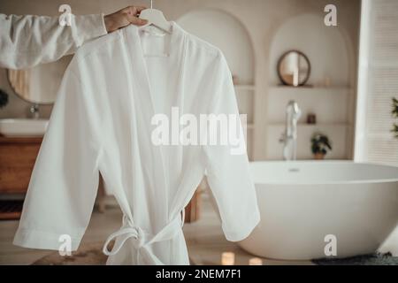 Le delicate sfumature native hanno un aspetto organico del bagno con grande finestra ovale vasca da bagno in tonalità neutre. Piante di palma verde candele bagnomaria leasure e rela Foto Stock