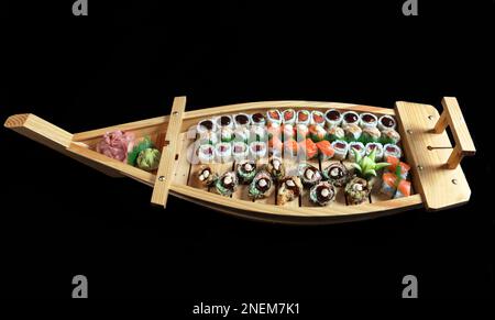 Un primo piano di delizioso sushi adagiato su un grande piatto di legno a forma di barca su uno sfondo nero Foto Stock