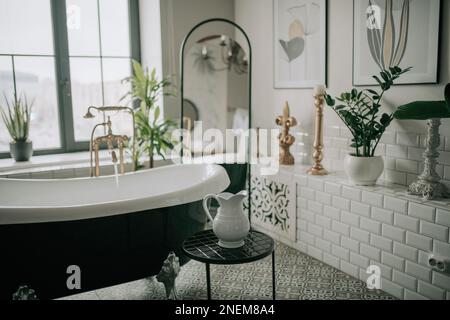 Colori nativi aspetto di forme organiche del bagno con grande finestra ovale vasca da bagno in toni terreni neutri. Piante di palma verde candele gorgoglibeble leasure e rel Foto Stock