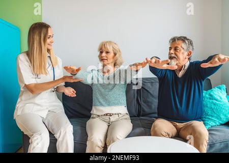 Donna caregiver assistere coppia anziana a casa di cura, mostrando loro alcuni esercizi Foto Stock