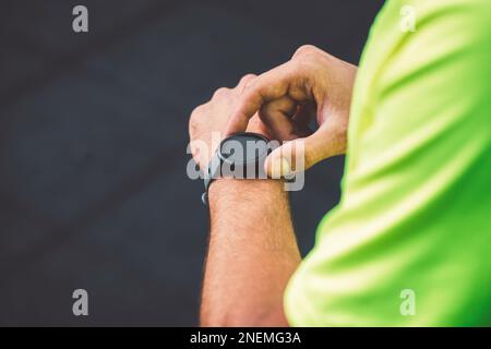 Primo piano uomo in camicia verde impostare la sua attività di orologio sportivo Foto Stock