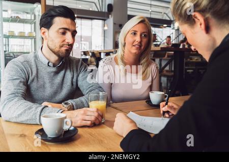 Giovane coppia in un incontro con un po' di caffè con il loro agente immobiliare Foto Stock