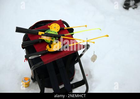 Persona irriconoscibile che tiene una canna da pesca di ghiaccio di plastica su un lago ghiacciato. Altre persone in lontananza Foto Stock