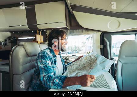 Libertà e stile di vita all'avanguardia. Un uomo felice di mezza età sorridente e che pianifica un viaggio su una mappa guida seduto all'interno di un camper casa a motore. Alte Foto Stock