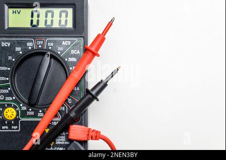 Vista dall'alto di uno strumento per il test dei circuiti elettrici. Multimetro digitale e puntali su sfondo bianco. Foto Stock