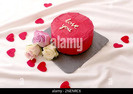 torta bento rotonda rossa, cuori e rose giacciono sul letto bianco di luce naturale Foto Stock