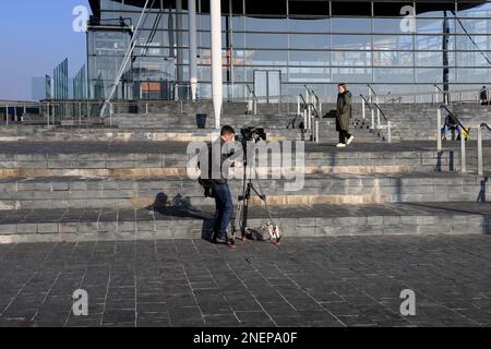 Filmare un pezzo-a-telecamera all'esterno dell'edificio Senedd, la baia di Cardiff. Uomo di macchina fotografica e intervistatore. Febbraio 2023. Inverno Foto Stock