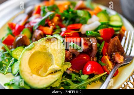 Insalata di verdure tritate su piatto bianco come cibo vegano fresco con rucola verde, pomodori heirloom, peperoni rossi e avocado mezzo macro closeup Foto Stock