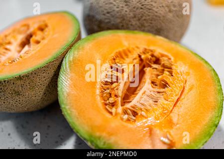 Melone di cantaloupe arancione colorato tagliato a metà con macrococchiatura a metà e semi di frutta succosa e intero sullo sfondo Foto Stock