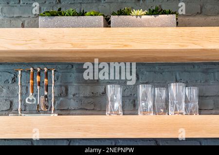 Mensole in legno della cucina con succulente piante in vaso verde, bicchieri da bere e porta-apribottiglie utensili contro muro di mattoni dipinti in casa Foto Stock