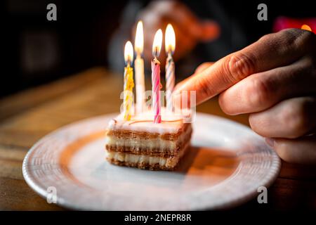 Torta francese napoletana fetta vista laterale primo piano su piatto bianco stratificato con crema e luce a mano candele di compleanno su piccolo dessert pasticceria Foto Stock