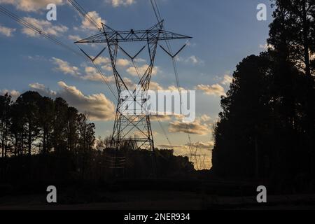 Silhouette di torre di trasmissione dell'elettricità al crepuscolo contro il cielo blu e le nuvole soffici. Foto Stock
