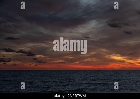 Vista del mare al crepuscolo contro un cielo sovrastante. Le nuvole catturano gli ultimi raggi rosso-arancio del sole che tramonta sul Mar Mediterraneo. Foto Stock