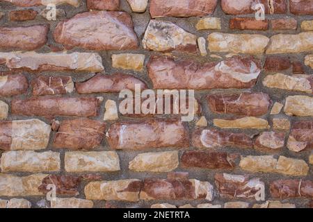 Sfondo a texture a cornice intera di un muro in pietra rustico costruito con blocchi di calcare naturale rosa e ocra e malta Foto Stock