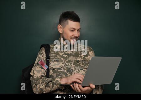 Cadet con zaino e computer portatile vicino alla lavagna. Educazione militare Foto Stock