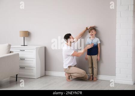 Padre che misura l'altezza del figlio vicino al muro di casa Foto Stock