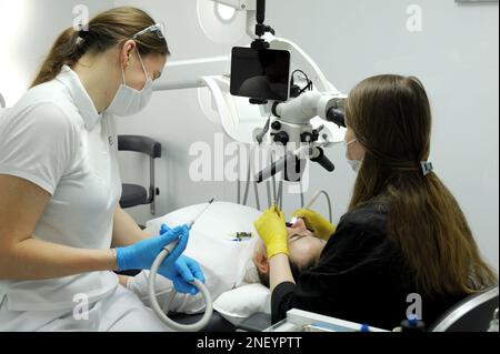 Attrezzatura odontoiatrica moderna tecnica di applicazione di guanti da dentista femmina con microscopio dentale per esaminare i denti dei pazienti medico paziente assistente trattamento dentale protesi Calipso scanner Foto Stock