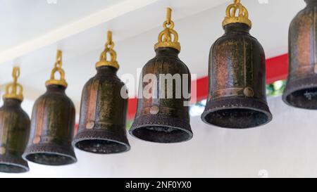 Sei campane tradizionali color bronzo appendono una dopo l'altra contro una parete bianca. Foto Stock