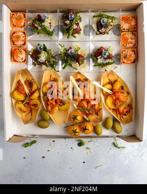 spuntini assortiti per il catering alla luce. tartare, bruschetta, insalate, patate, tartine da consegnare in scatola di cartone Foto Stock