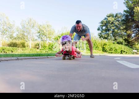 Ragazza che gioca con il padre mentre pattina a rotelle all'aperto nel parco. Foto Stock