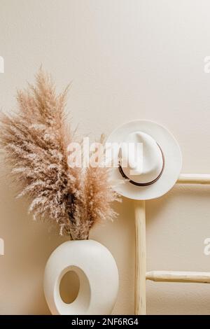 Erba secca di pampas nel vaso, scala di legno con cappello. Interni boho Foto Stock